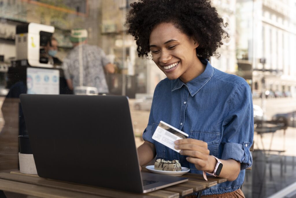 Mulher sorridente segurando um cartão de crédito em frente ao notebook, em um café